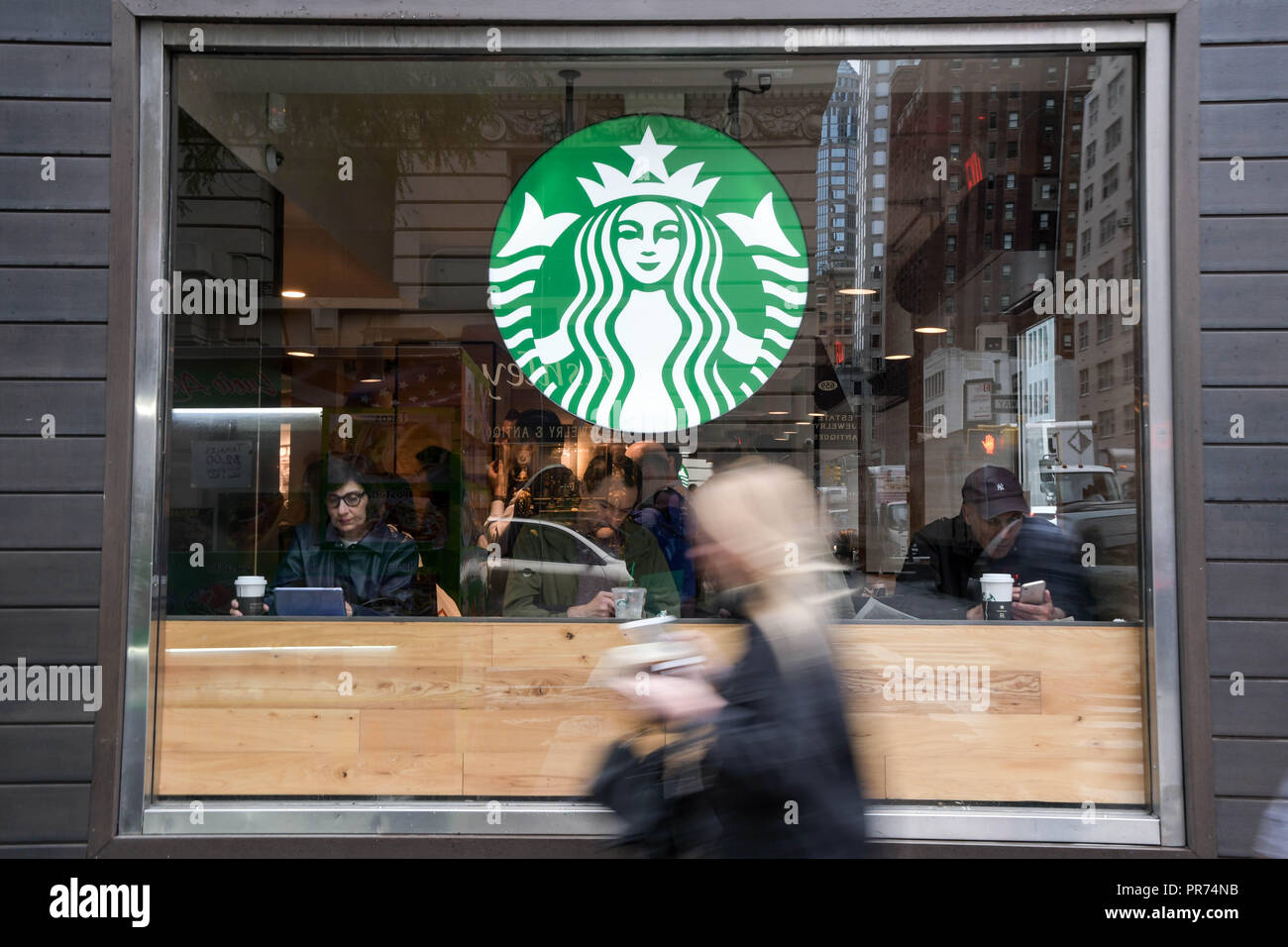 Una donna cammina davanti a uno Starbucks sulla Fifth Avenue a New York City in un nuvoloso mattina di settembre. Foto Stock