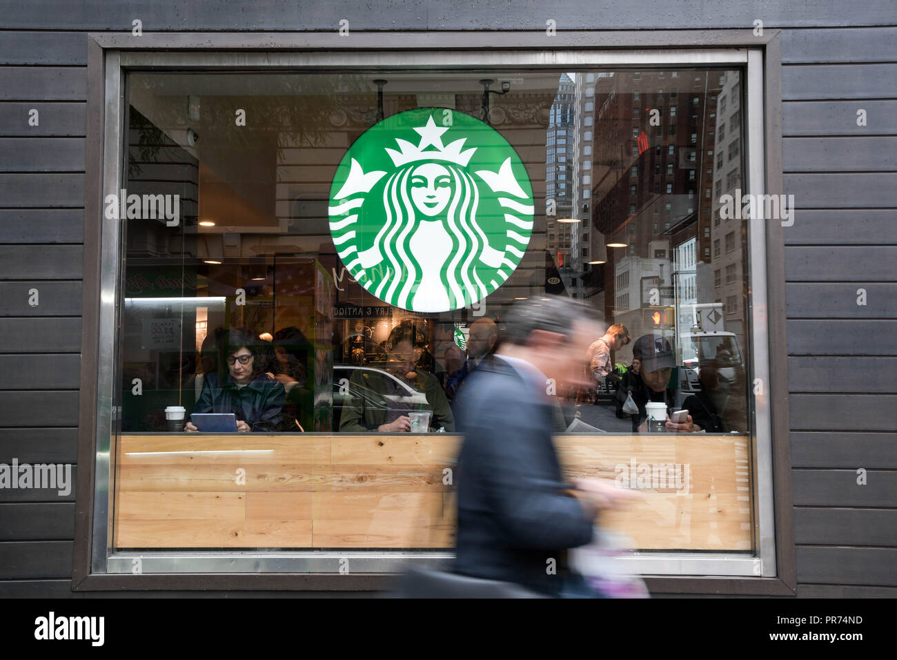 Un imprenditore controlla il telefono cellulare mentre si cammina passato uno Starbucks sulla Fifth Avenue a New York City in un nuvoloso mattina di settembre. Foto Stock