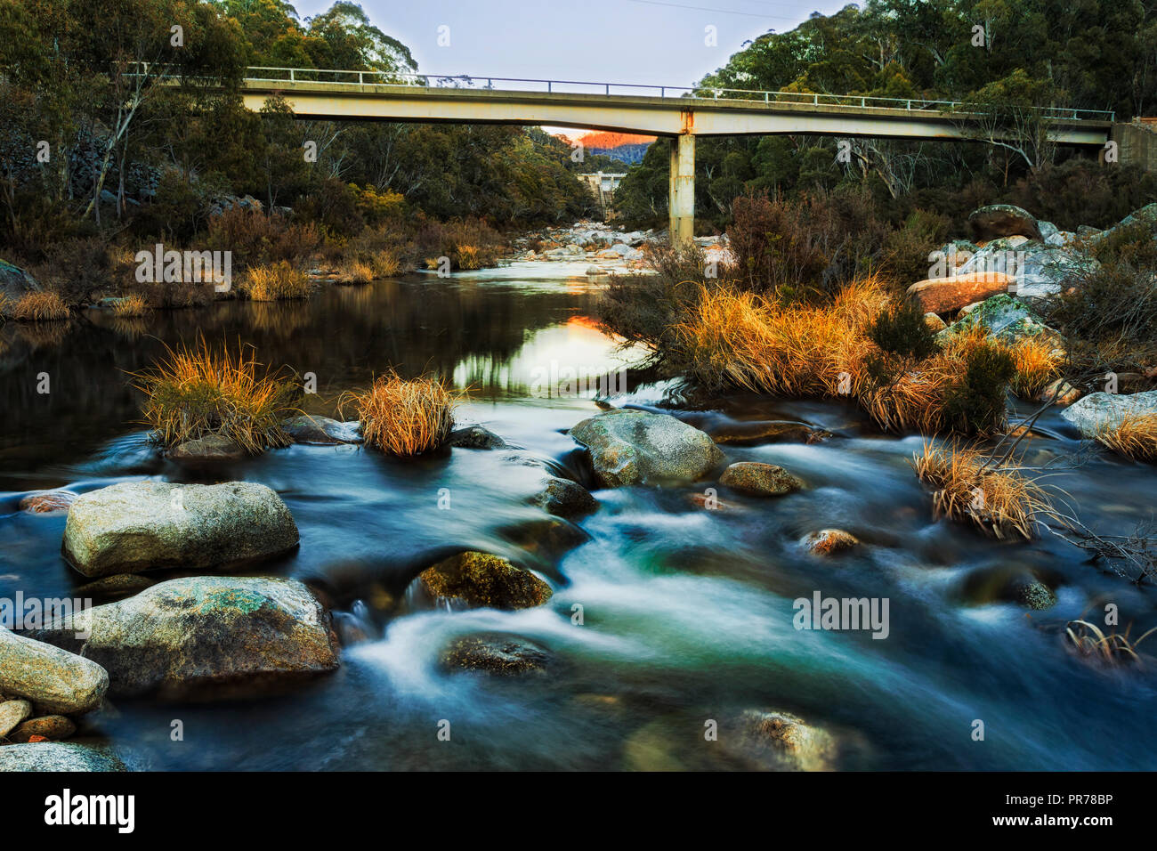 Sfocata acque a freddo su terreni innevati fiumi durante il congelamento stagione invernale sotto Gathega dam in montagne innevate dell Australia che scorre tra massi. Foto Stock