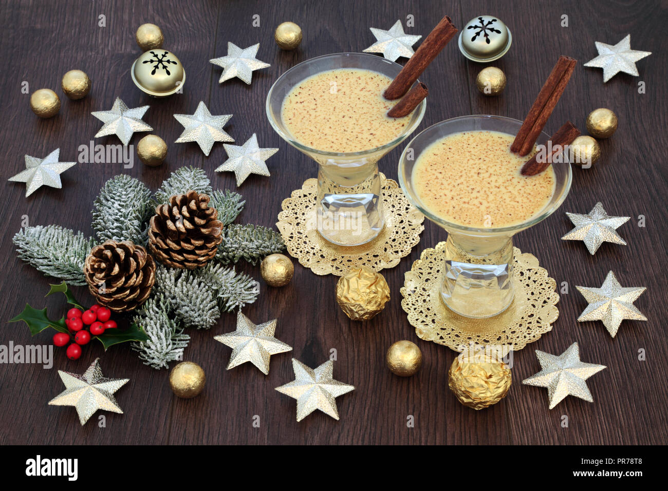 Zabaione tradizionale drink di Natale con stella in oro e decorazioni a campana, stagnola avvolto le sfere di cioccolato, con flora invernale di holly, abete e pigne Foto Stock