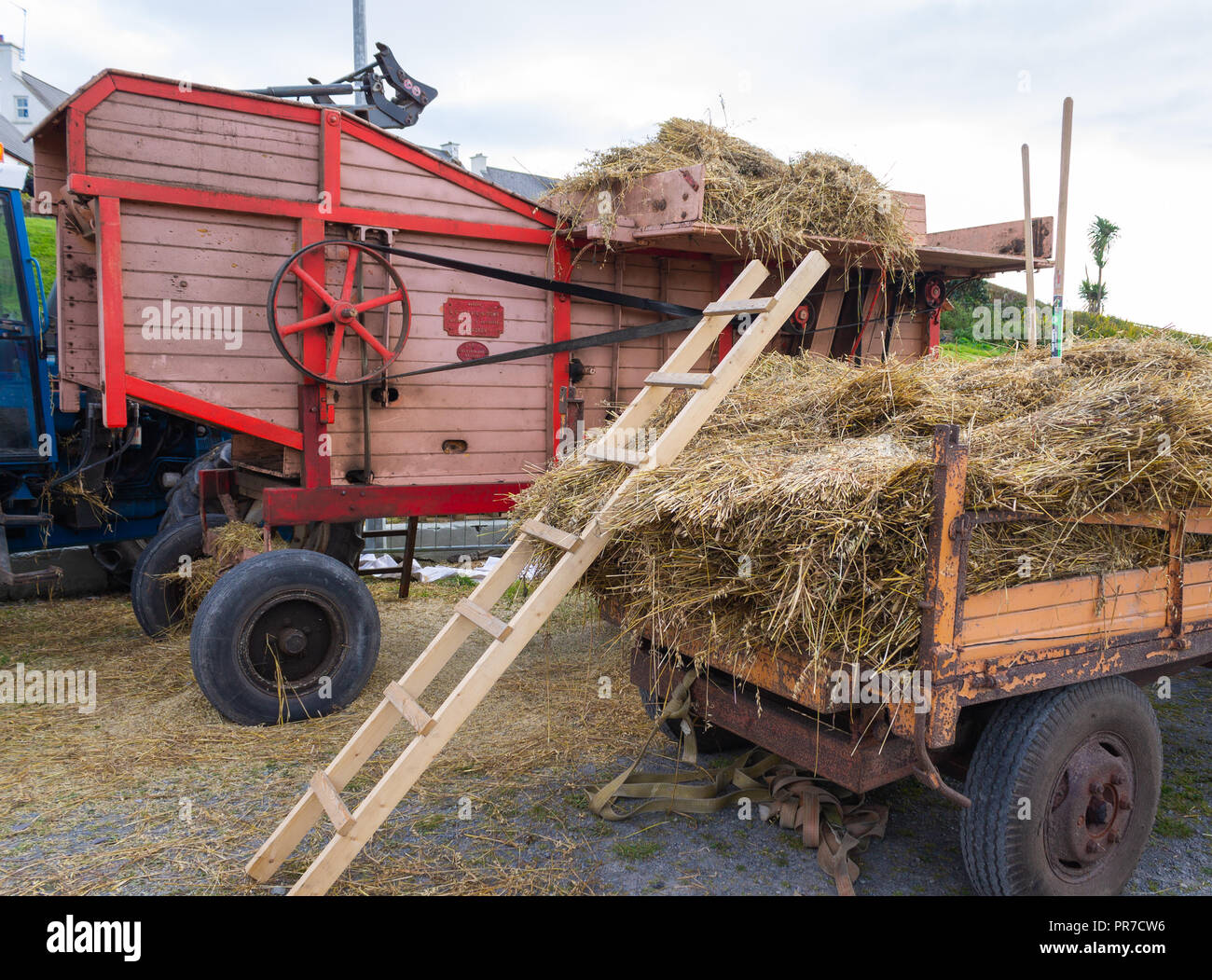 Trebbiatura vintage macchina vicino a un carrello pieno di covoni di avena in un paese giusto. Foto Stock