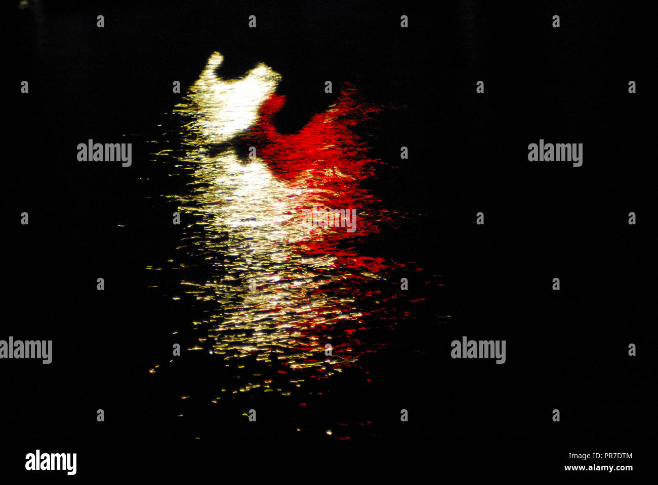 Riflessi scintillanti di rosso e golden lights on dark acqua crea un meraviglioso sfondo per qualsiasi presentazione multimediale. Nota l'ombra nella forma di Foto Stock