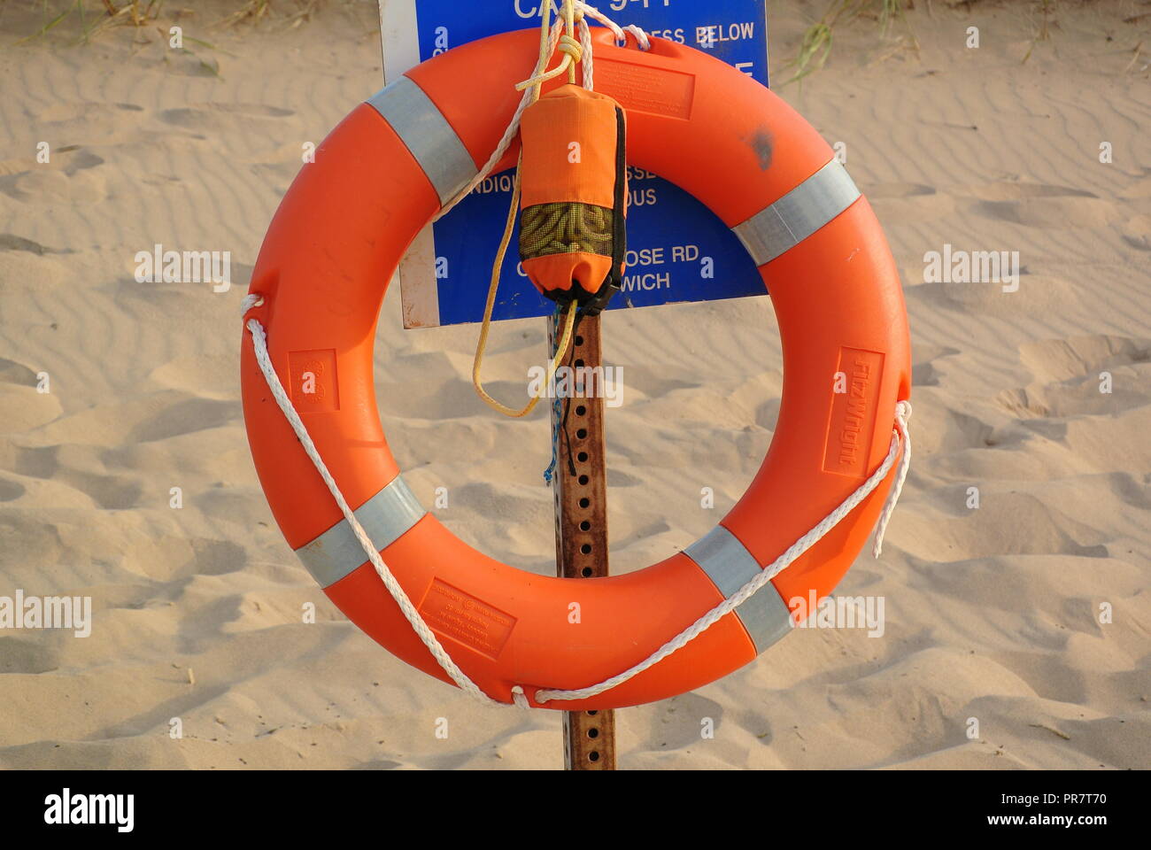 Close-up di un arancio anello di sicurezza (BOA) e bagnino corda appesa sulla rastrelliera metallica con un metallo targhetta di avvertenza su un rosso spiaggia sabbiosa, Canada Foto Stock