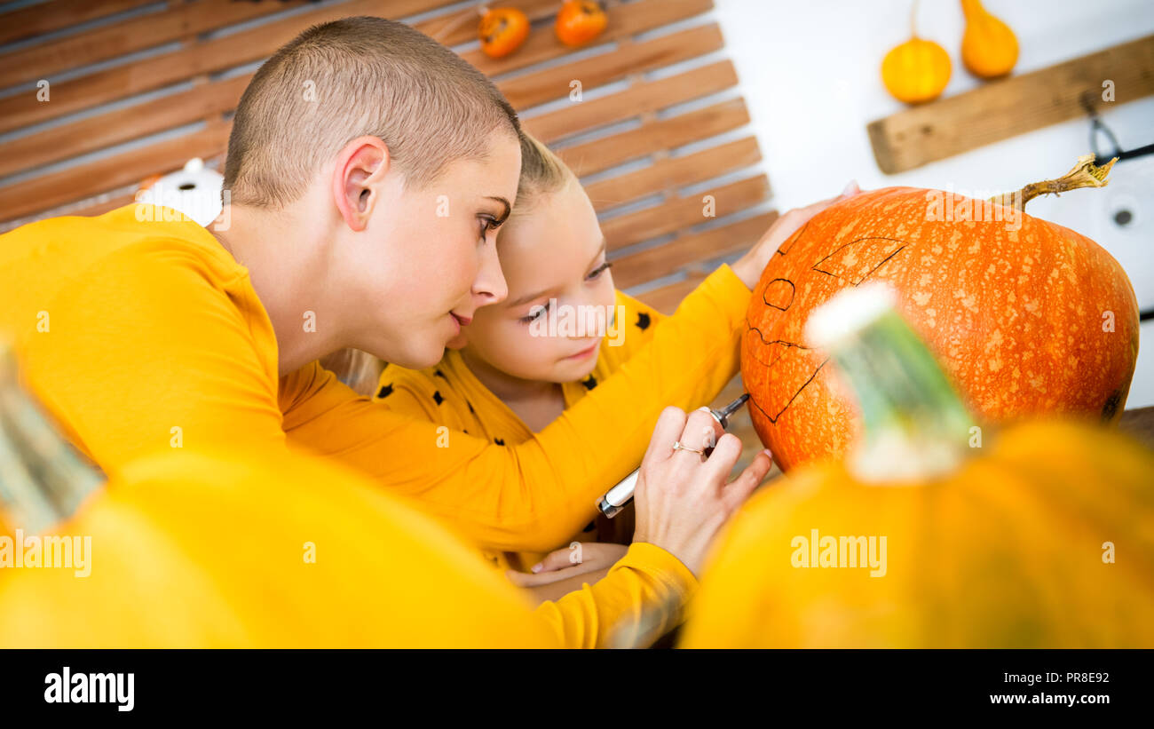 Madre e figlia di disegno antropomorfi smiley; faccia su una grande zucca di Halloween. Famiglia decorare la zucca. Foto Stock