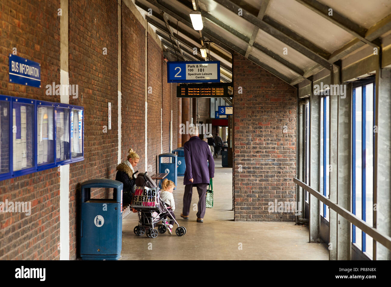 Donna con bambino nel passeggino e titolare di pensione o di rendita camminare davanti a Guildford stazione degli autobus Foto Stock