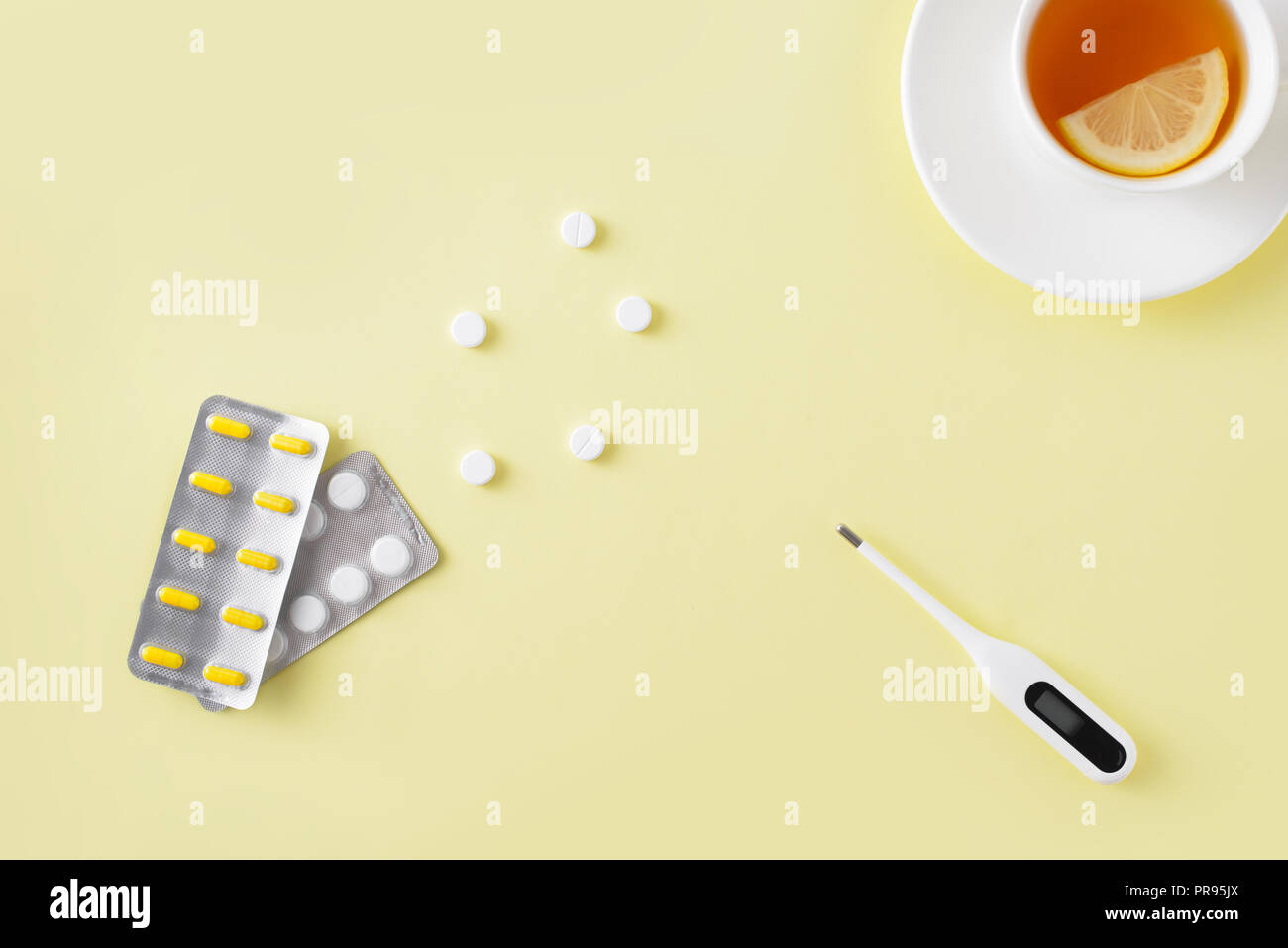 Pillole, termometro e tazza di tè su sfondo giallo. Raffreddore e influenza il trattamento impostato. Appartamento laico, vista dall'alto. Copia gratuita dello spazio. Foto Stock