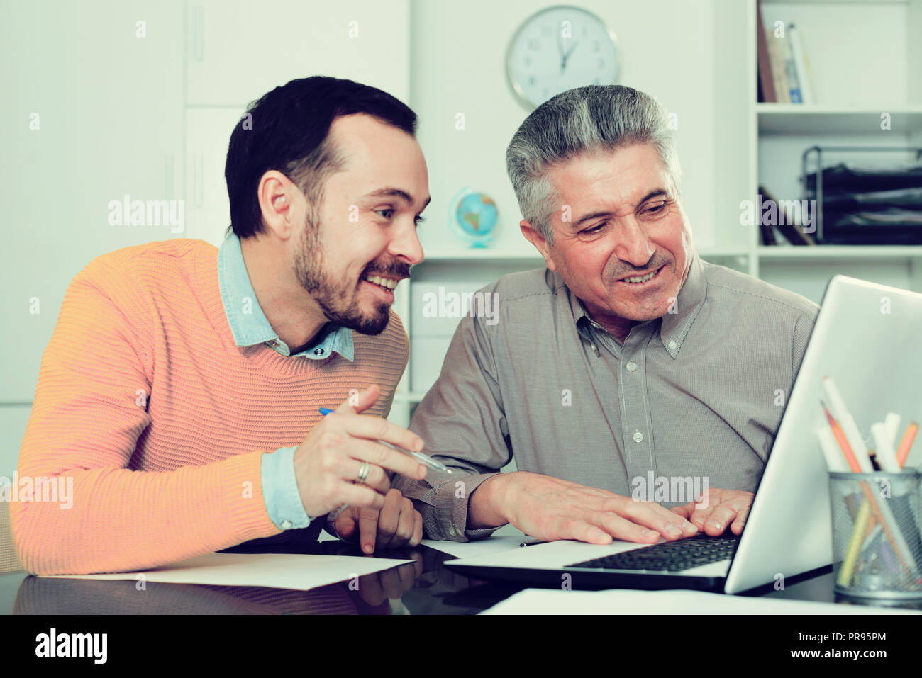 Sorridente per adulti e giovani uomini hanno un aspetto interessante su Internet sul computer portatile alla reception a ofice Foto Stock