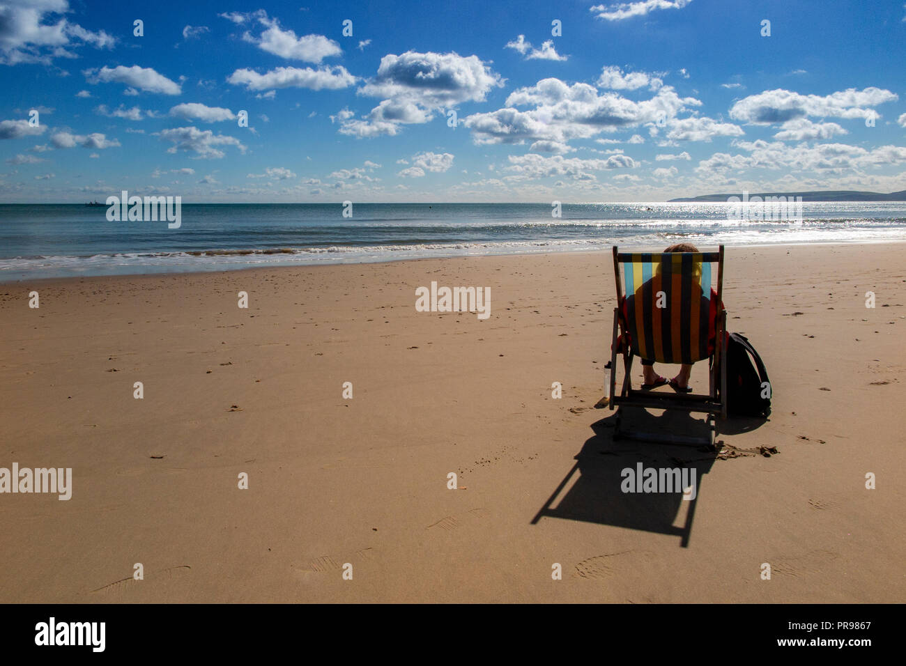 Un lone persona gode della solitudine, seduto in una sedia a sdraio con una spiaggia tutta per se stessa - nessuno lì, solo la possibilità di sedersi e di sogno Foto Stock