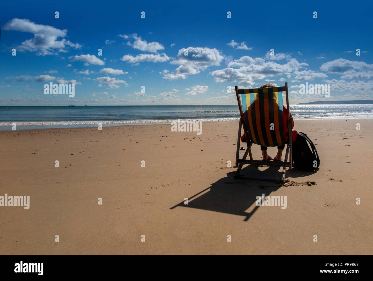 Un lone persona gode della solitudine, seduto in una sedia a sdraio con una spiaggia tutta per se stessa - nessuno lì, solo la possibilità di sedersi e di sogno Foto Stock