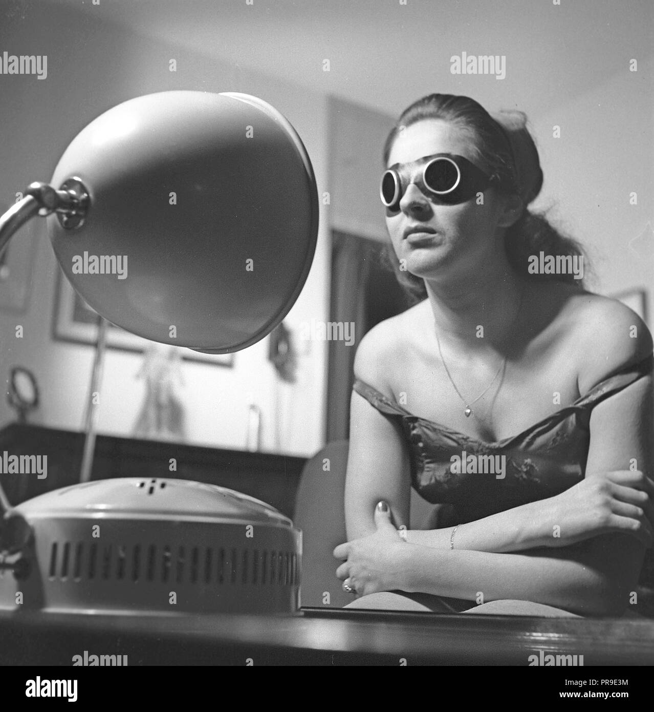 Bellezza negli anni '1940s. Una giovane donna sta prendendo un'abbronzatura davanti ad una lampada solare. La luce artificiale del sole dalle apparecchiature di abbronzatura domestiche come questa lampada da sole ha dato un'abbronzatura ed era a volte un trattamento per le malattie. Durante l'uso, è necessario indossare occhiali da sole protettivi. Svezia 1947. Foto Kristoffersson Y81-3 Foto Stock