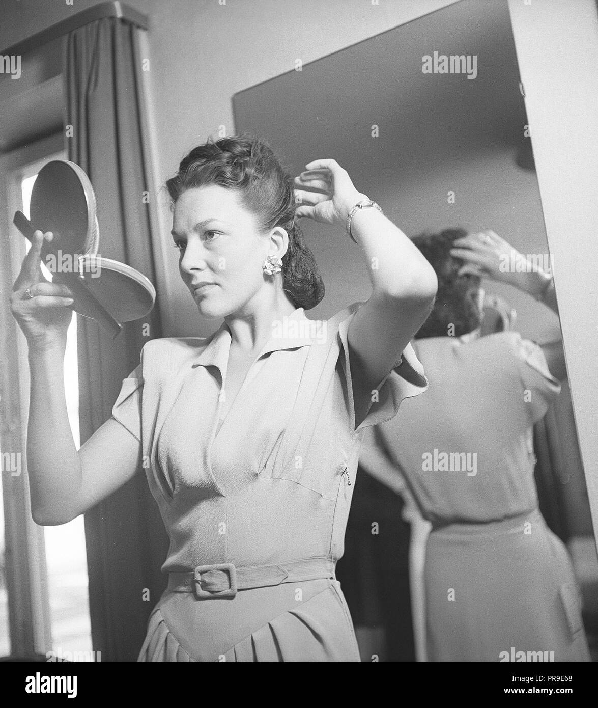 Donna che fissa i capelli negli anni '1940s. Una giovane donna dai capelli scuri si sta guardando in uno specchio da tasca mentre fissa i suoi capelli. Svezia 1947. Foto Kristoffersson Ref U118-2 Foto Stock