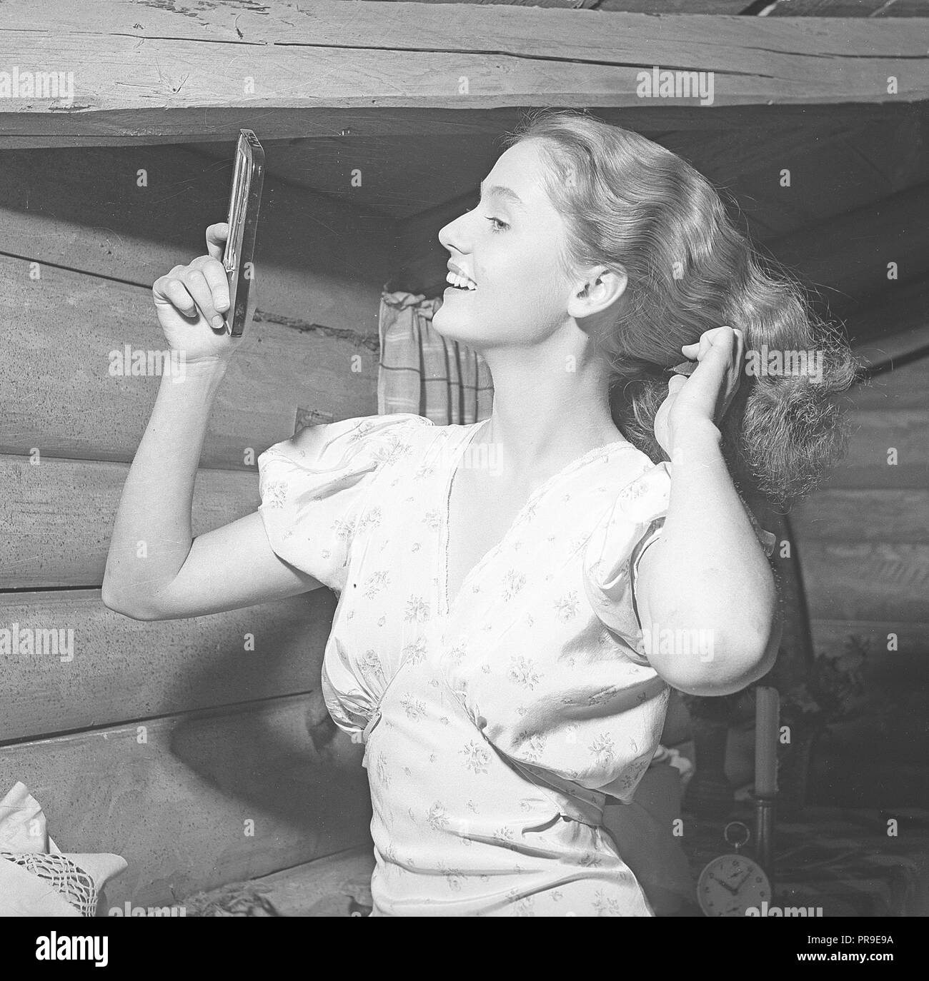 Donna che fissa i capelli negli anni '1940s. Una giovane donna bionda si guarda in uno specchio da tasca mentre pettina i capelli. Svezia 1945. Foto Kristoffersson Ref P146-4 Foto Stock