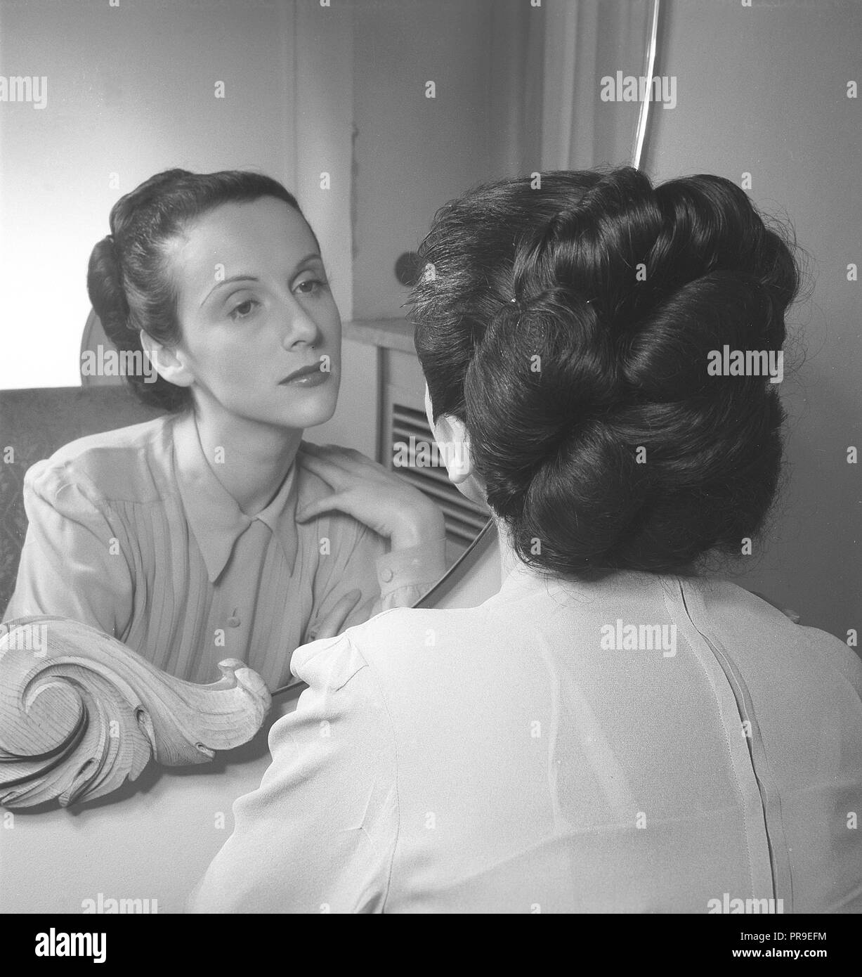 La donna nel 1940s. Un giovane dai capelli scuri donna è seduta davanti allo specchio e guardando se stessa. La Svezia 1940s. Foto Kristoffersson ref T79-5 Foto Stock