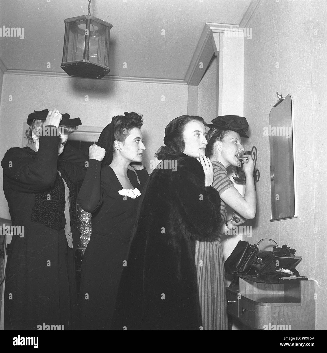 Le donne si prepara per una notte fuori nel 1940s. Il gruppo di quattro donne stanno rendendo il tocco finale per i loro capelli e vestiti e il trucco. Essi sono tutti cercando di ottenere un assaggio di sé nel piccolo specchio sulla parete. La Svezia 1944. Foto Kristoffersson ref M93-6 Foto Stock