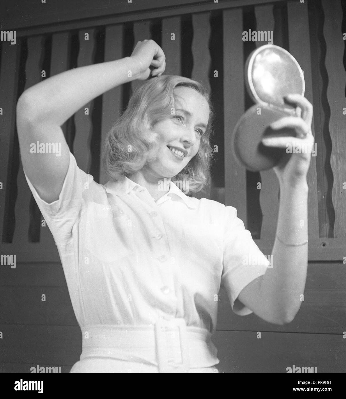 Donna che fissa i suoi capelli nel 1940s. Una giovane donna bionda sta guardando a se stessa in un specchio tascabile mentre pettinare i capelli. La Svezia 1943. Foto Kristoffersson ref F7-4 Foto Stock