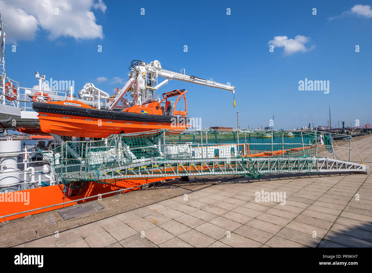 Un motore di colore arancione sloop pende sul lato della nave e la passerella è sulla banchina. Foto Stock