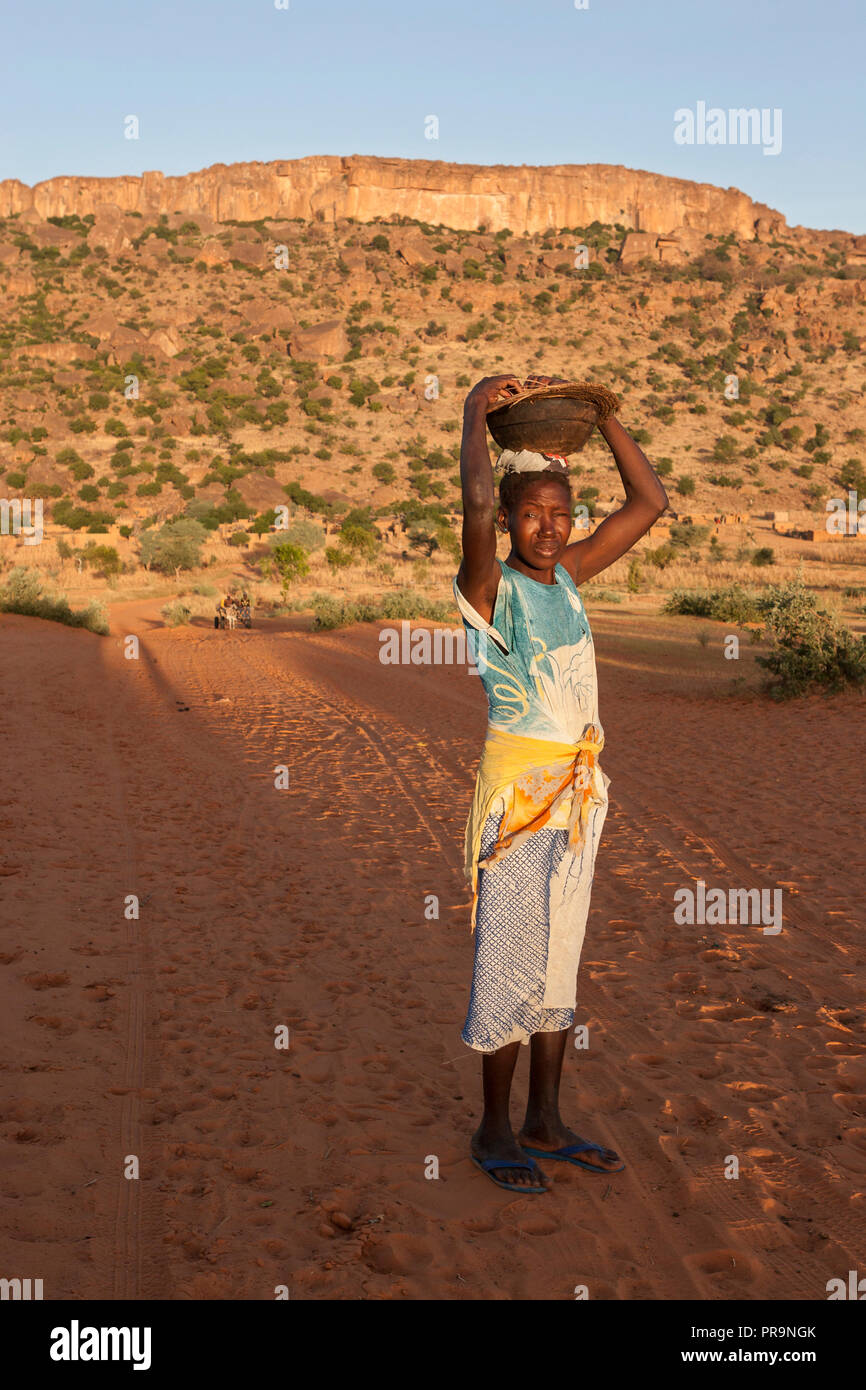 Donna africana che porta una ciotola di legno sulla sua testa davanti di Bandiagara scarpata Foto Stock