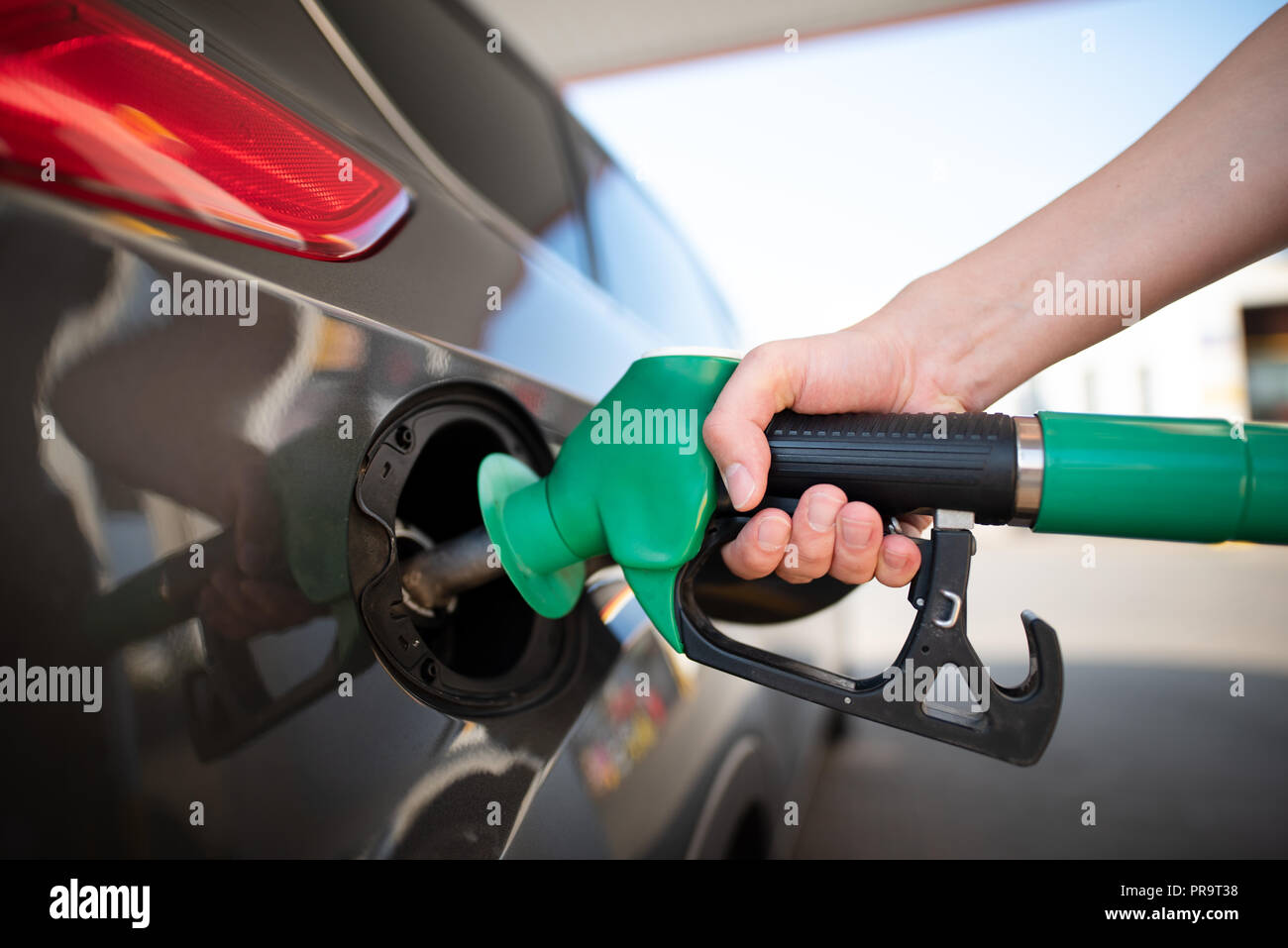 Closeup dell uomo di pompaggio del carburante benzina in auto alla stazione di gas. Gas ugello della pompa nel serbatoio del carburante di una vettura di colore grigio Foto Stock