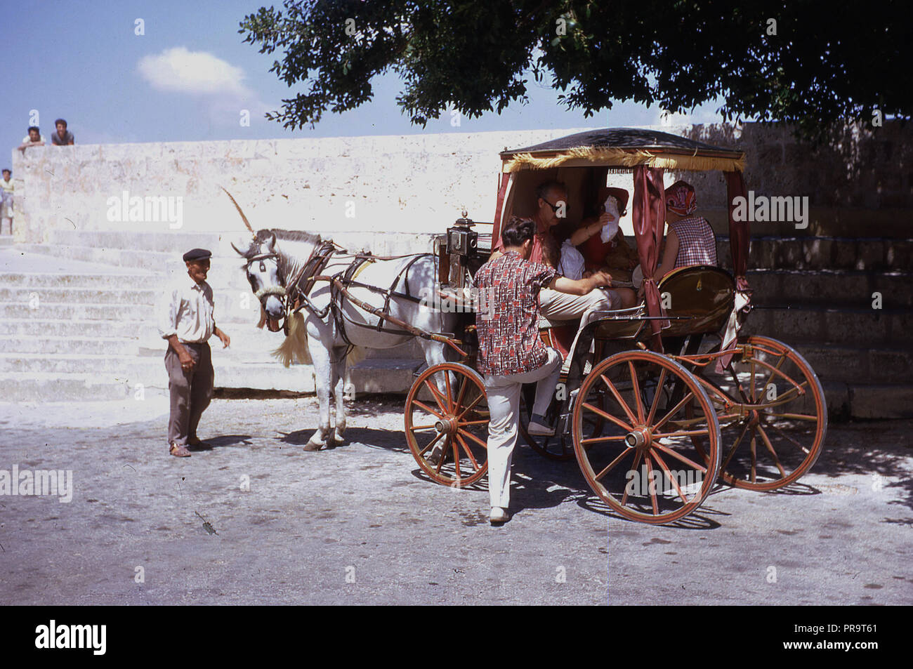 Anni sessanta, storico adulti turisti in Malta ottenendo un giro in un tradizionale a cavallo il decoro quattro ruote di trasporto. Foto Stock