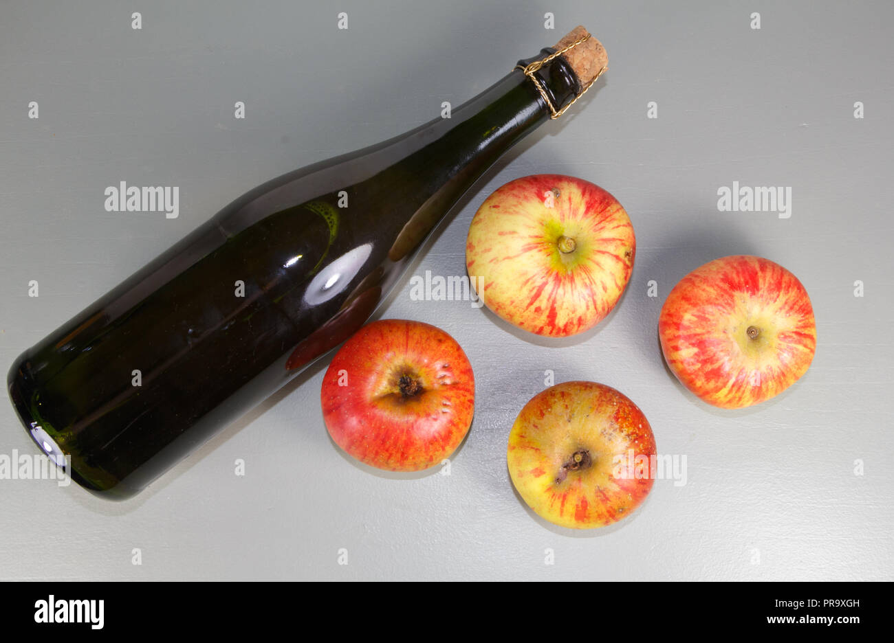 Quattro di rosso e di giallo mele vicino a una bottiglia di sidro da Brittany Foto Stock