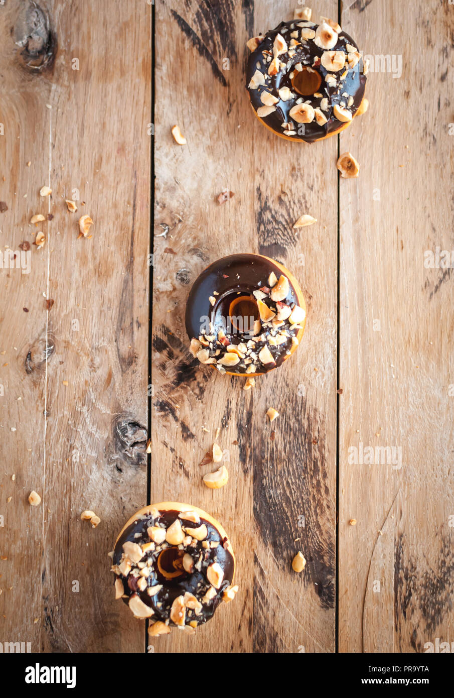 Cioccolato ciambelle vetrata con le nocciole su sfondo di legno, vista dall'alto Foto Stock