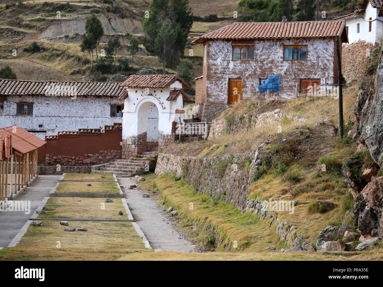 La scena del villaggio con muri in pietra e porte ad arco, tile case dal tetto ed erba Foto Stock