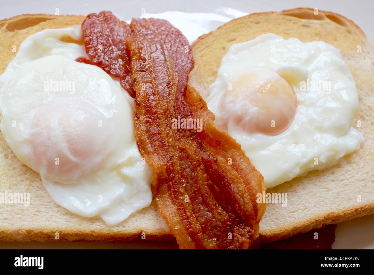 Le uova in camicia con croccante di pancetta su bianco unbuttered toast Foto Stock
