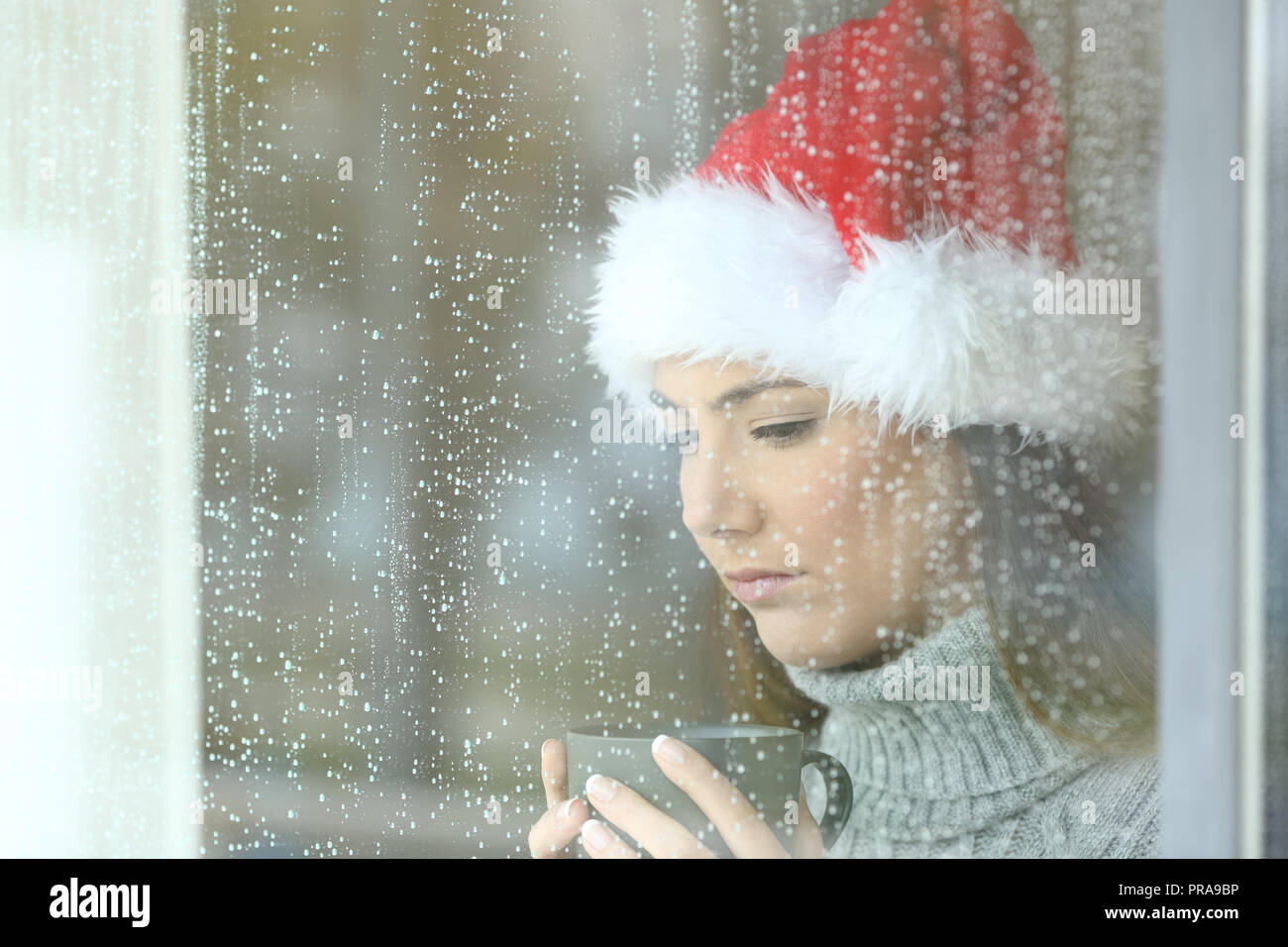 Triste la donna a Natale guardando verso il basso attraverso una delle finestre in un giorno di pioggia Foto Stock