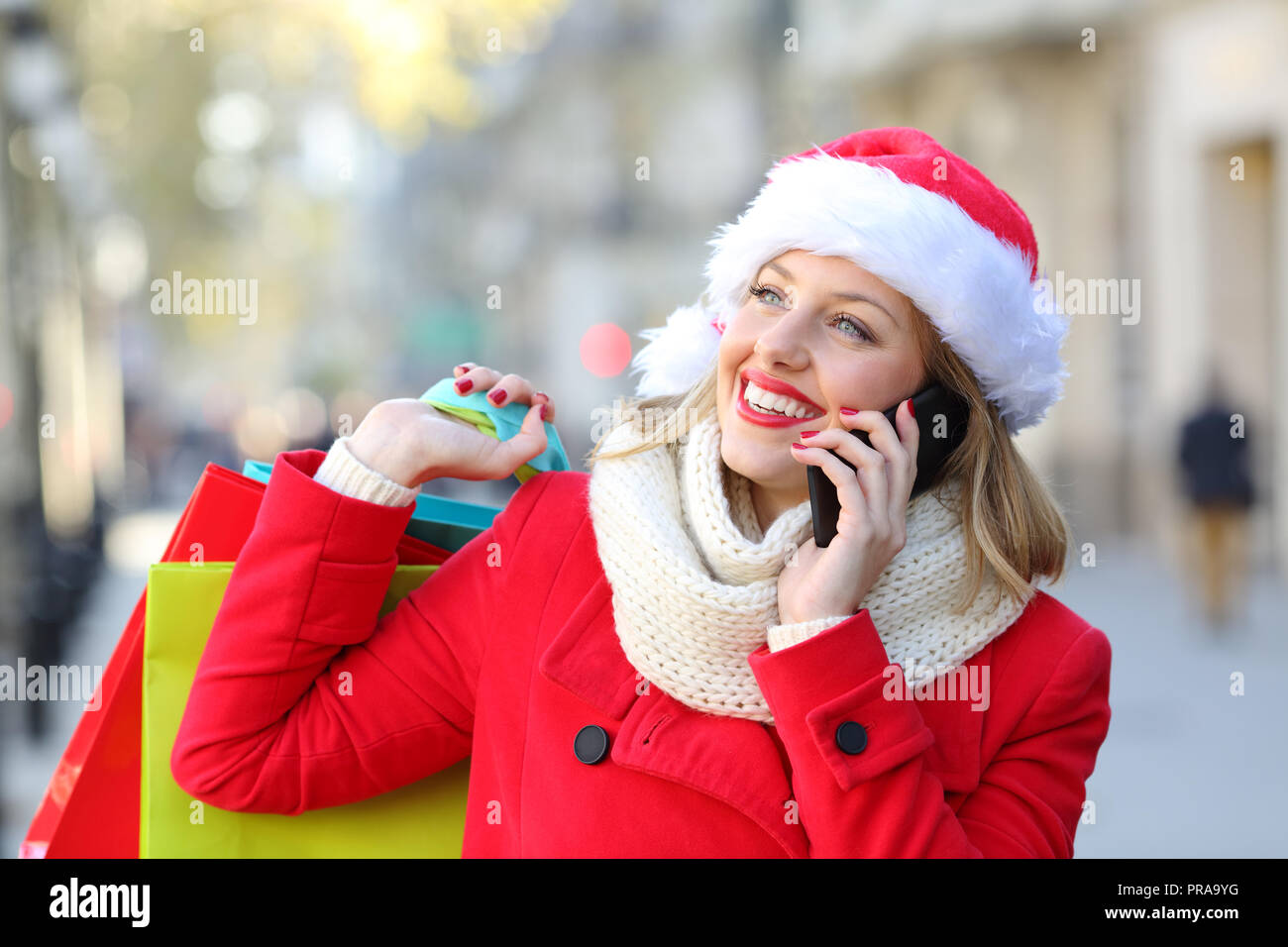Happy shopper in rosso azienda shopping bags parlando al telefono su vacanze di Natale sulla strada Foto Stock