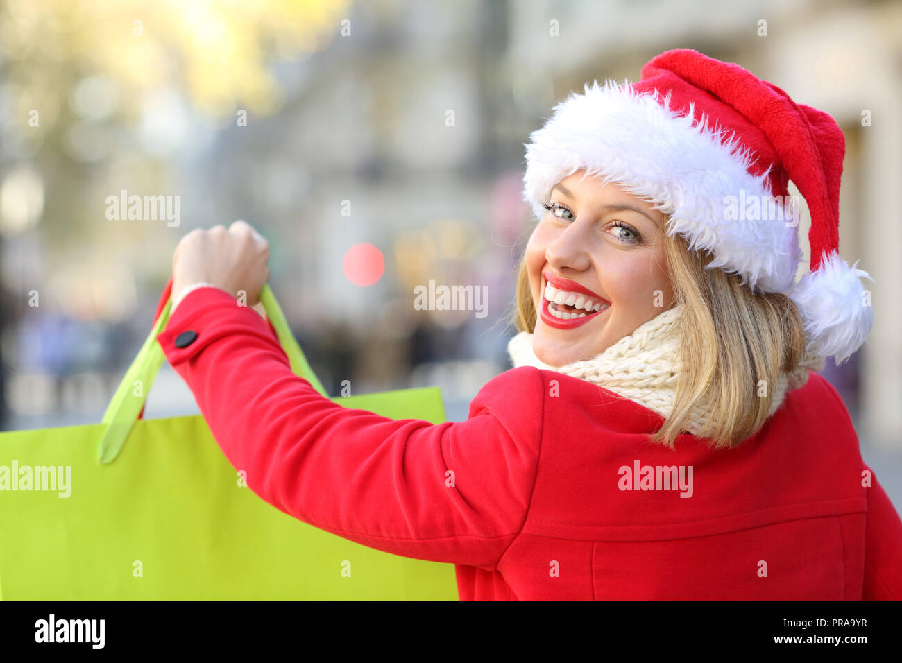 Ritratto di una donna felice shopping a Natale che indossa un berretto di Babbo Natale all'aperto sulla strada Foto Stock