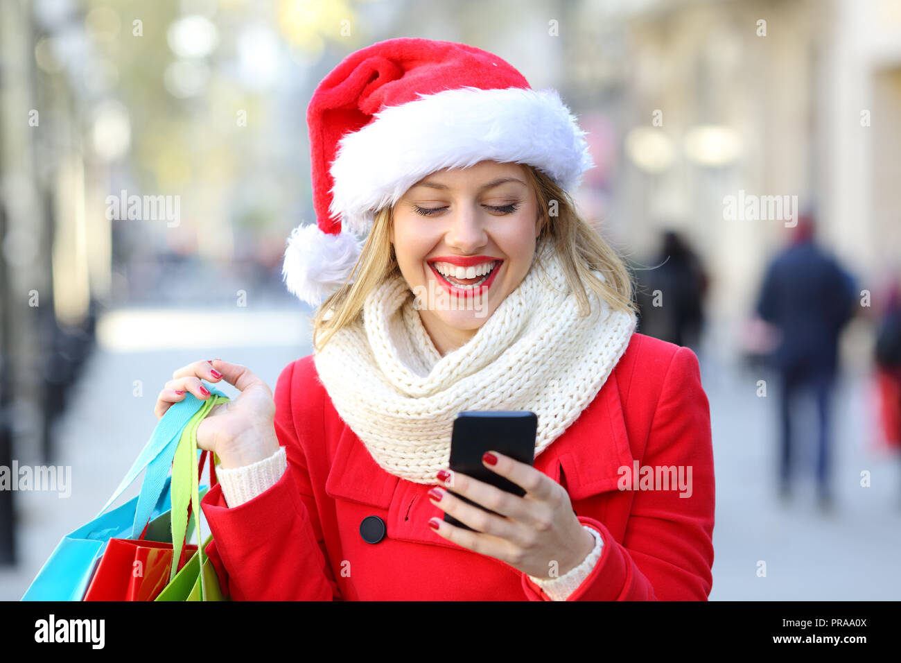 Vista anteriore verticale di un felice azienda shopper shopping bags controllo telefono sul Natale in strada Foto Stock