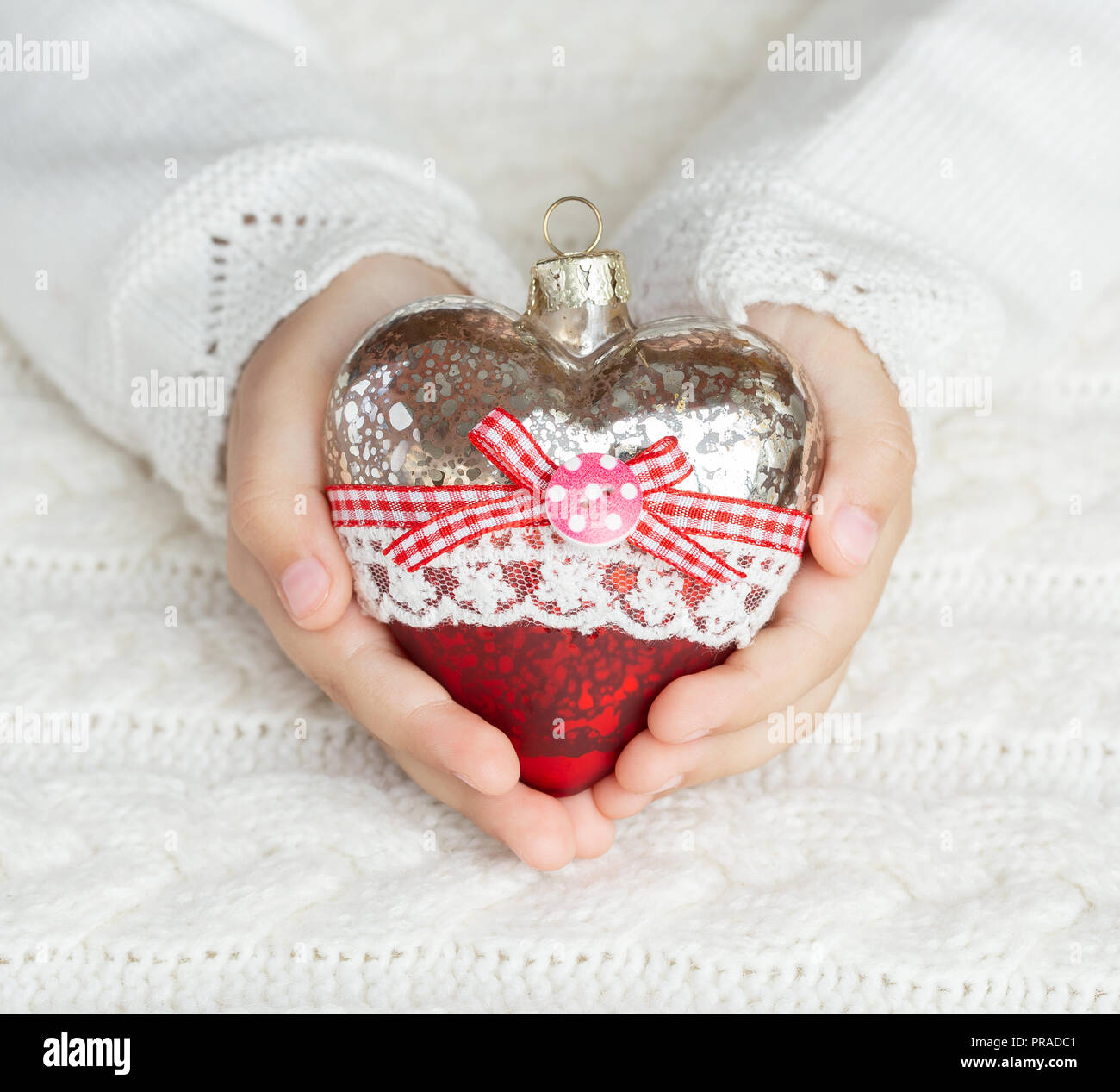 Bambino tiene un cuore di vetro, un giocattolo di Natale nelle mani sullo sfondo di un maglione caldo Foto Stock