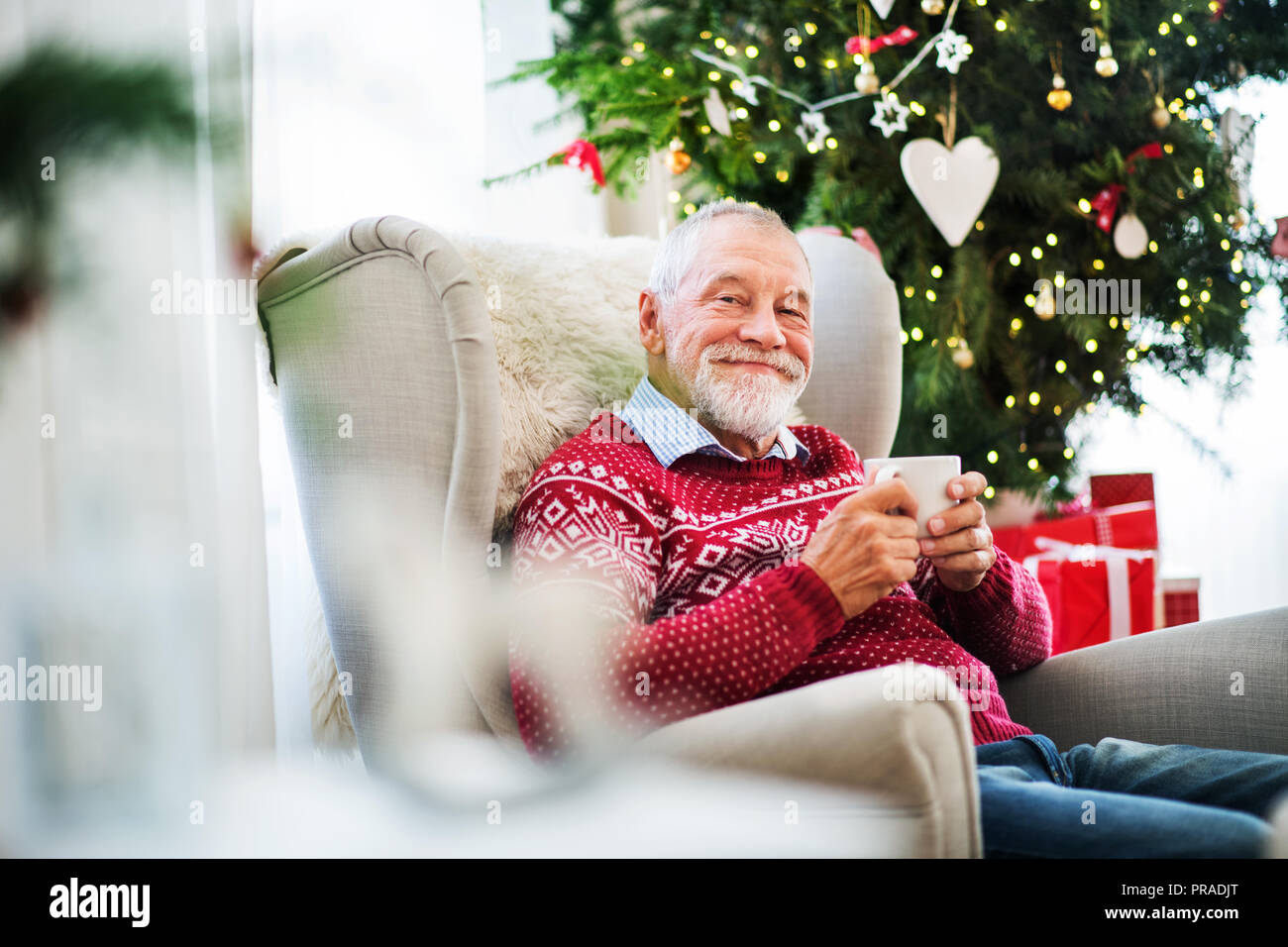 Un ritratto di uomo anziano con una tazza seduti sulla poltrona di casa al tempo di Natale. Foto Stock