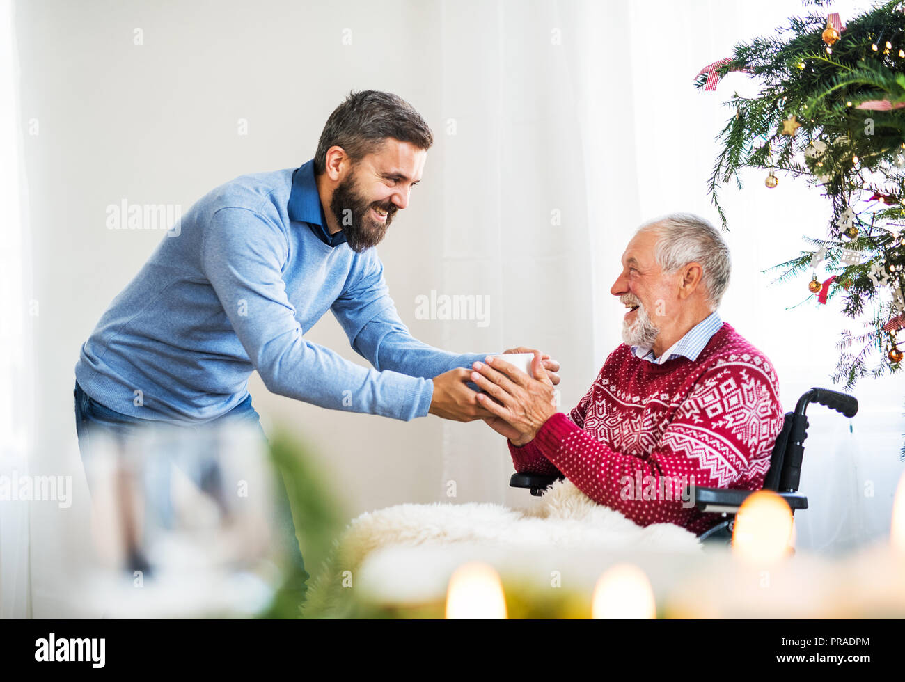 Un hipster man dar da bere al suo padre senior in sedia a rotelle al tempo di Natale. Foto Stock