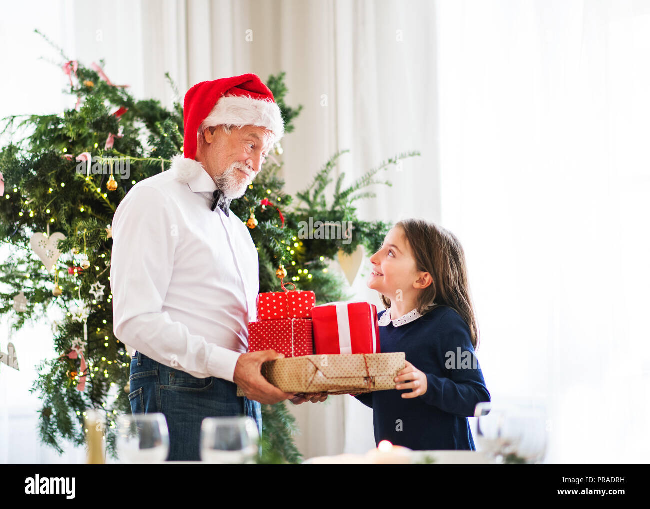 Un uomo anziano con un cappello da Babbo Natale dando presenta una piccola ragazza al tempo di Natale. Foto Stock