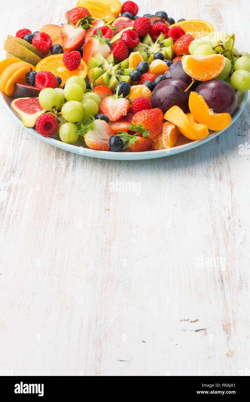 Una sana frutta, fragole lamponi arance Prugne Mele Kiwi uve, mirtilli bianco sul tavolo di legno, verticale, spazio di copia Foto Stock