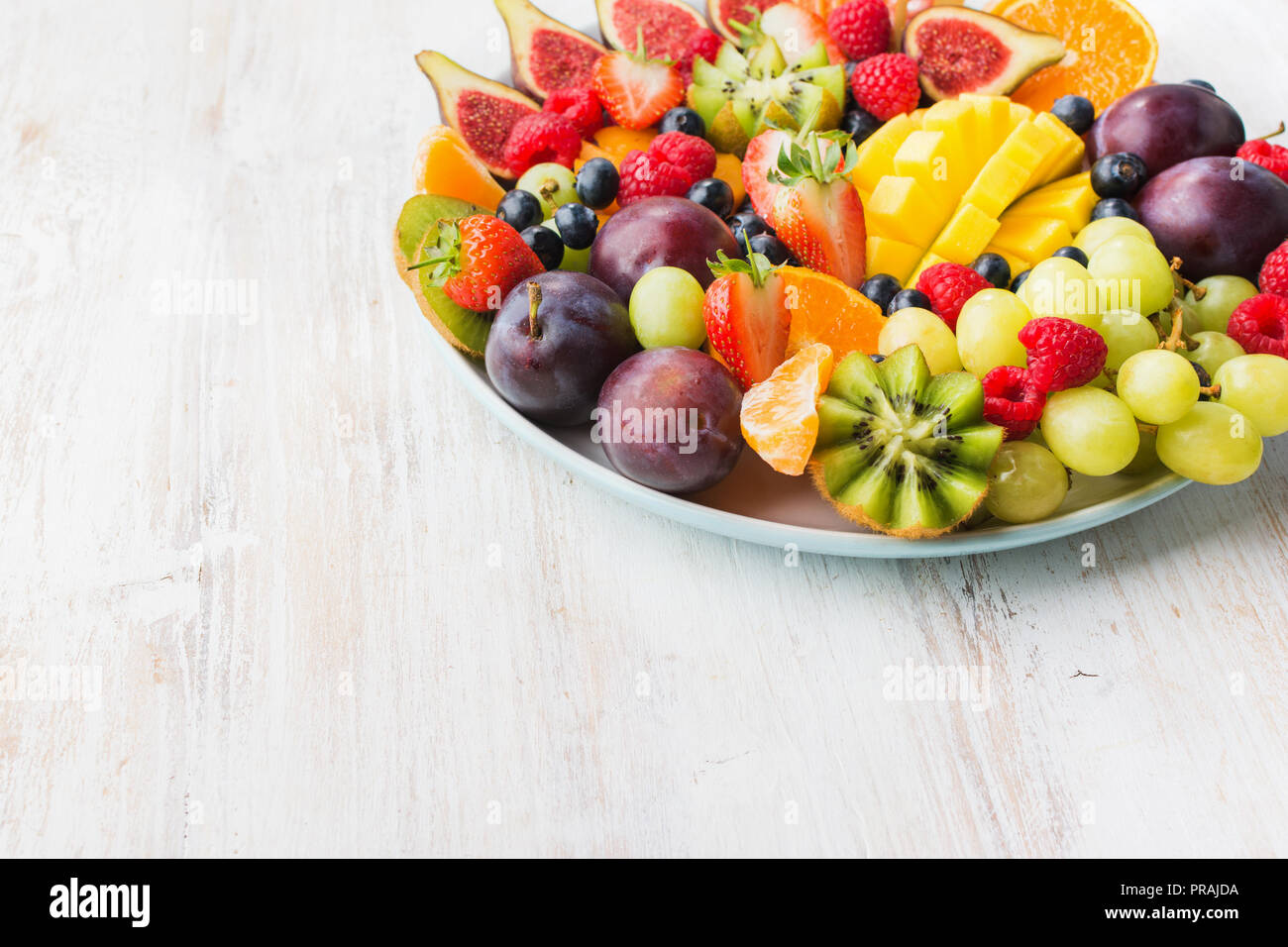 Raw sani frutti e bacche di piastra, Fragole Lamponi arance Prugne Mele Kiwi uve mirtilli, mango sul bianco woorden tabella Foto Stock