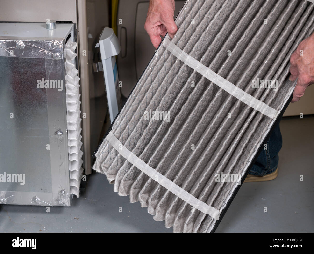 Uomo senior di cambiare un filtro dell'aria sporco in un forno HVAC Foto Stock