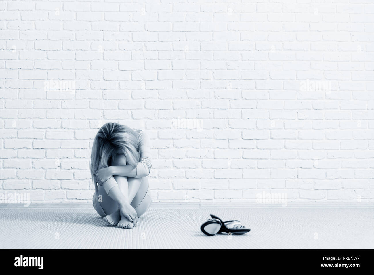 Triste giovane donna seduta sul pavimento vicino a un muro di mattoni. Foto Stock