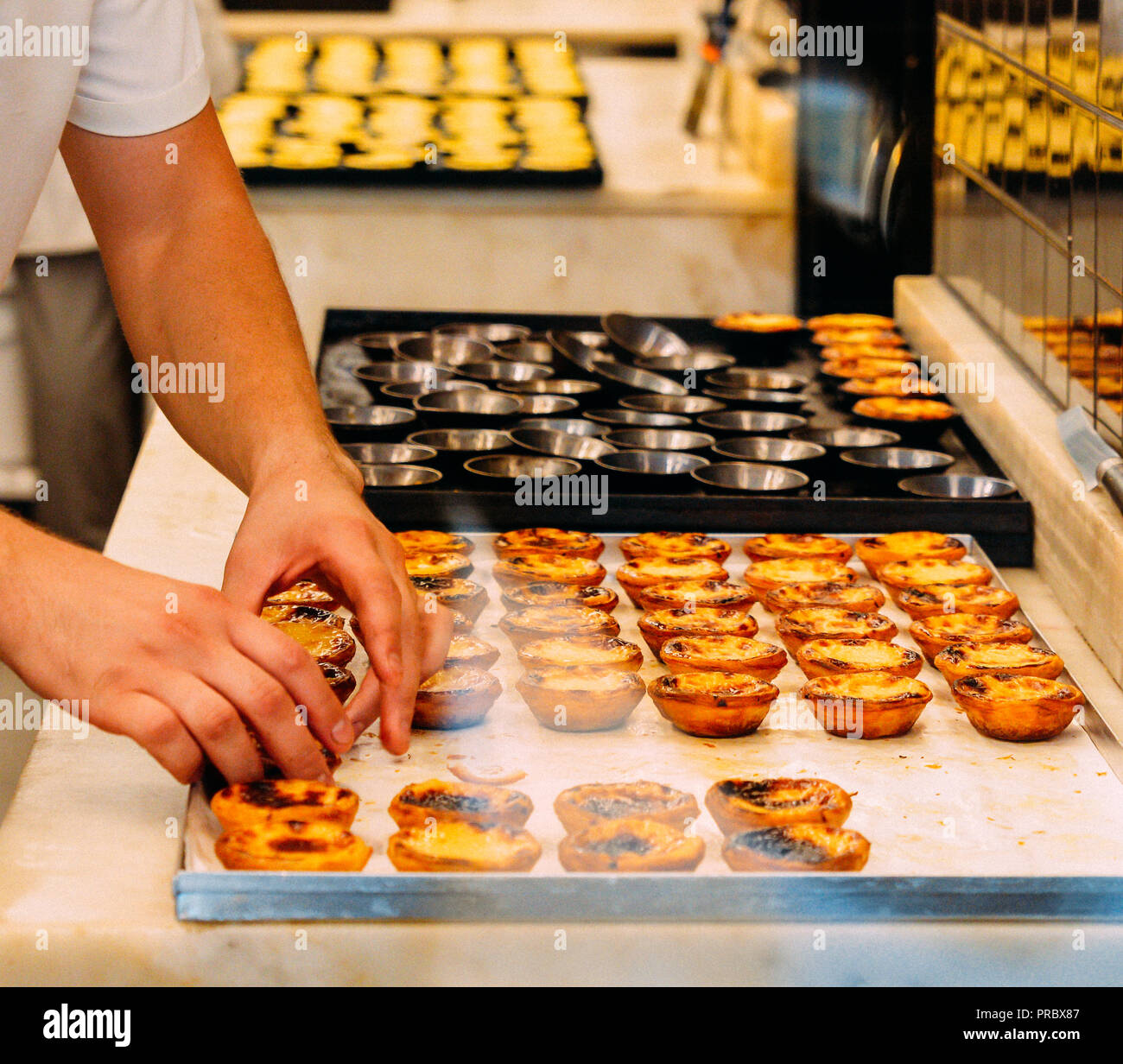 Lavoratore organizzare file di fresco uova cotte tart, tradizionale dolce portoghese, Pastel de nata, crema pasticcera crostate. Foto Stock