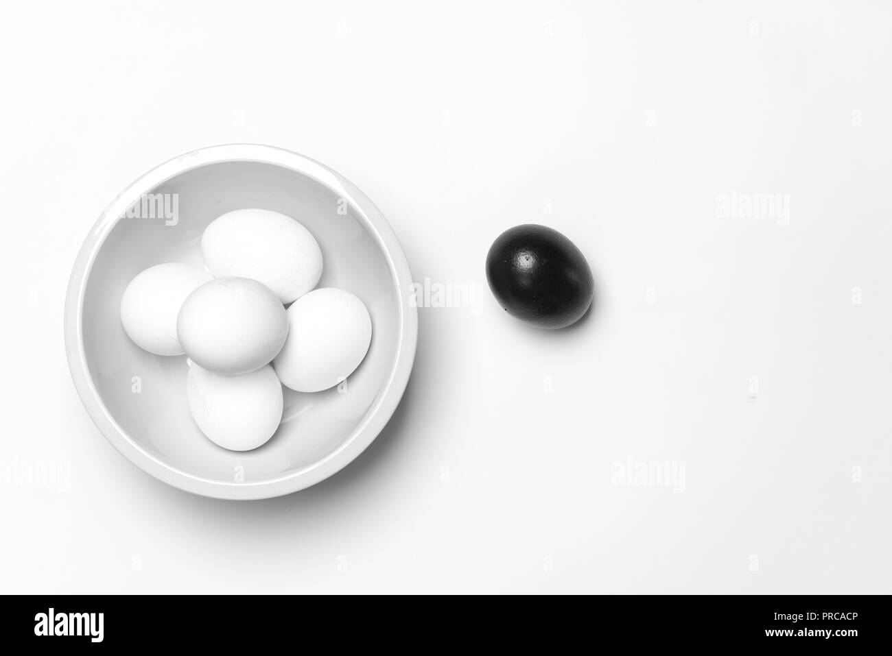 Su uno sfondo bianco, a pochi le uova bianche uno nero che simboleggia la diversità, separazione e leadership Foto Stock