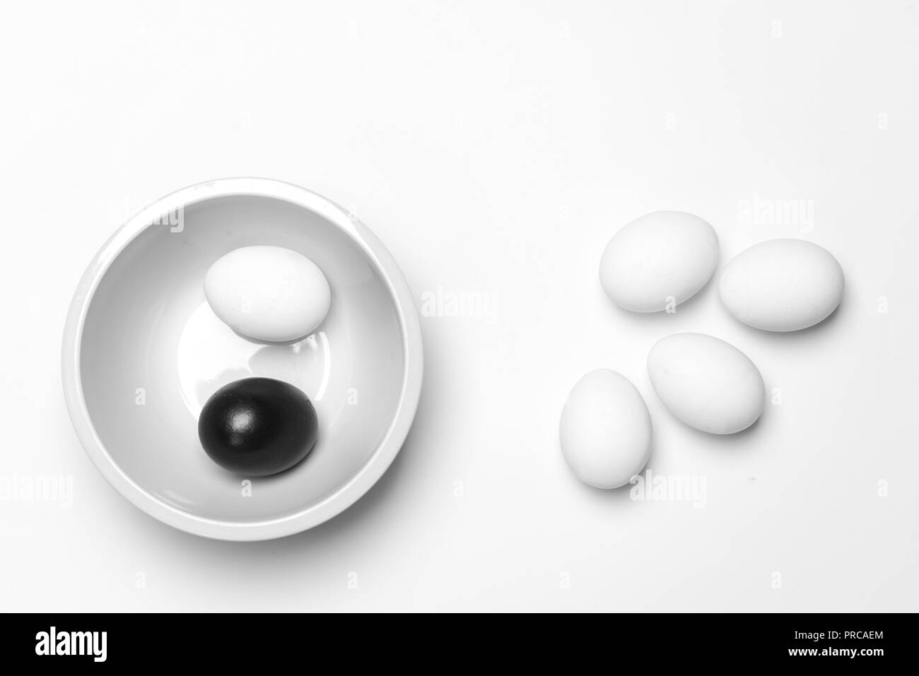 Su uno sfondo bianco, a pochi le uova bianche uno nero che simboleggia la diversità, separazione e leadership Foto Stock