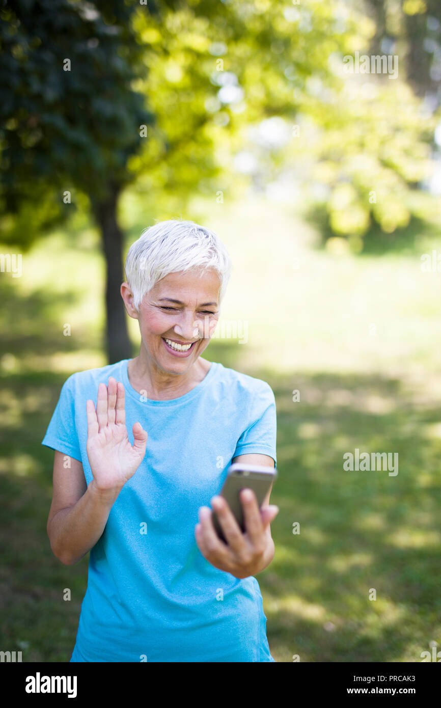 Ritratto di sportivo da donna senior utilizzando il telefono cellulare nel parco Foto Stock