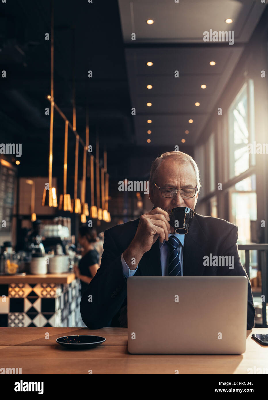 Colpo verticale di imprenditore senior guardando laptop e un caffè al caffè. Uomo maturo in business suit seduti al tavolo del bar con laptop drinkin Foto Stock