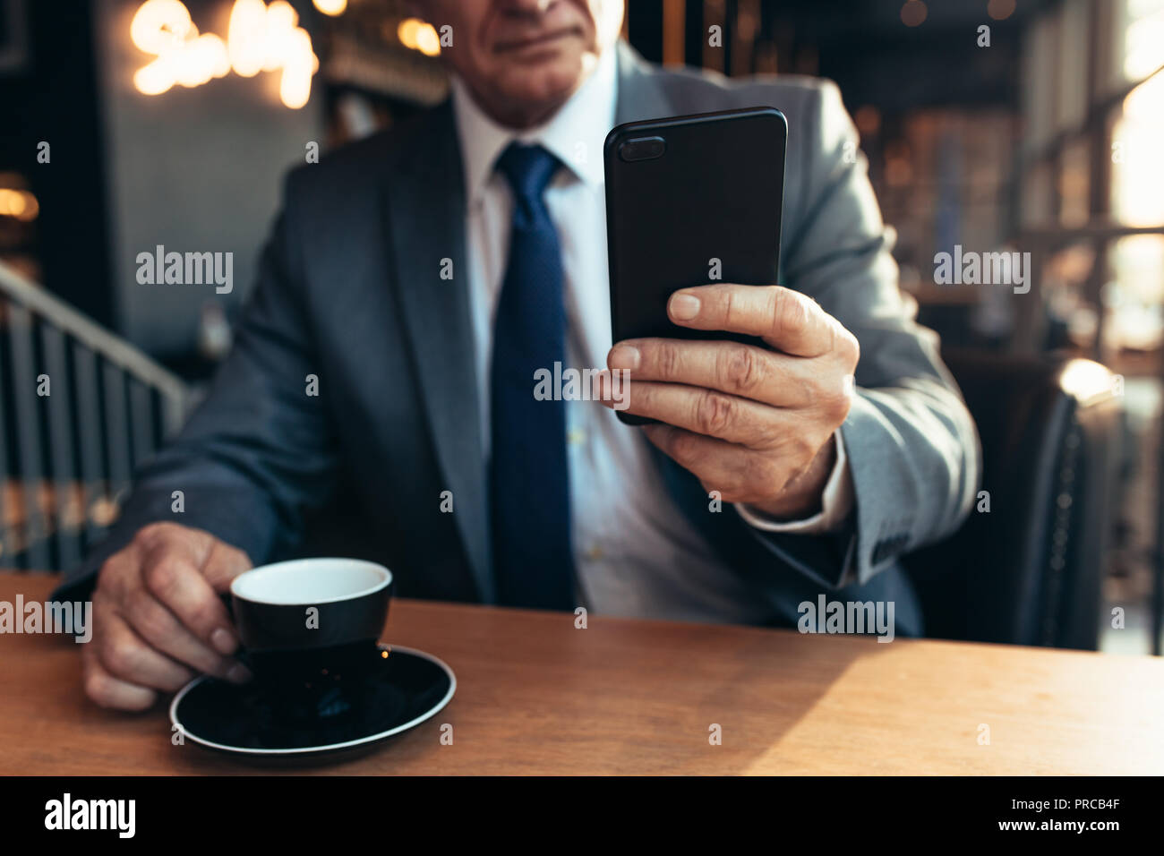 Chiusura del telefono cellulare nella mano di un uomo d affari con caffè sul tavolo del bar. Imprenditore Senior utilizza lo smartphone al coffee shop. Foto Stock