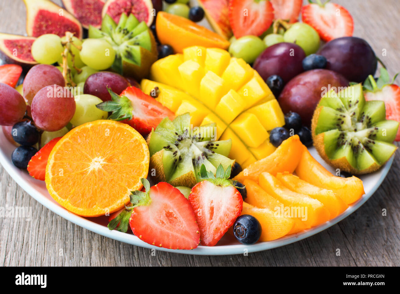 Un assortimento di frutti e bacche platter, fragole mirtilli, mango orange, Apple, uva da tavola, kiwi sul grigio Sfondo di legno Foto Stock