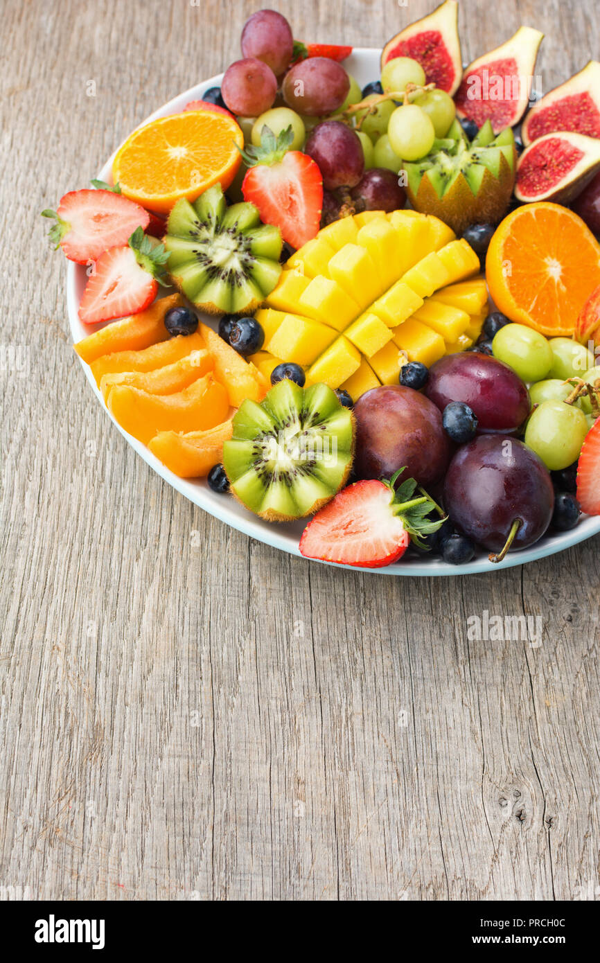 Un assortimento di frutti e bacche platter, fragole mirtilli, mango orange, Apple, uva da tavola, kiwi sul legno grigio Sfondo, spazio copia, verticale Foto Stock