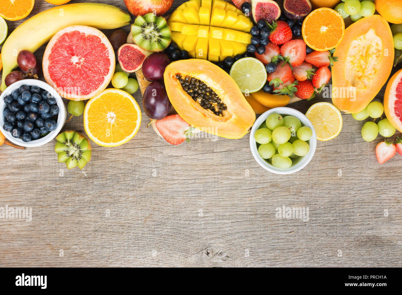 Vista superiore del rainbow frutti, fragole mirtilli, mango orange, pompelmo, banana papaya apple, uva da tavola, kiwi su grigio Sfondo legno, spazio di copia Foto Stock