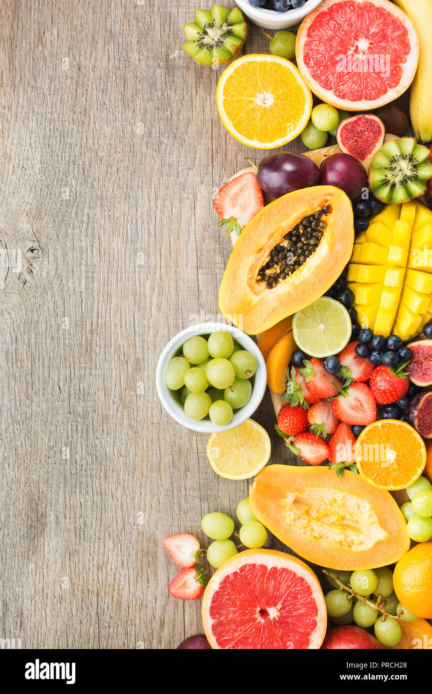Vista superiore del rainbow frutti, fragole mirtilli, mango orange, pompelmo, banana papaya apple, uva da tavola, kiwi su uno sfondo di legno, spazio di copia Foto Stock