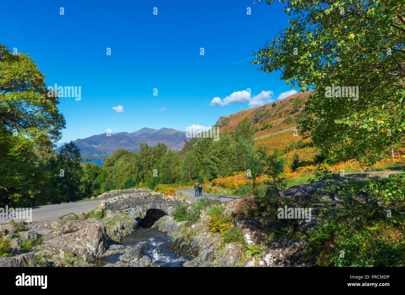 Coppia di mezza età a piedi a ponte Ashness con Skiddaw massiccio in distanza, Borrowdale, Lake District, Cumbria, Regno Unito Foto Stock